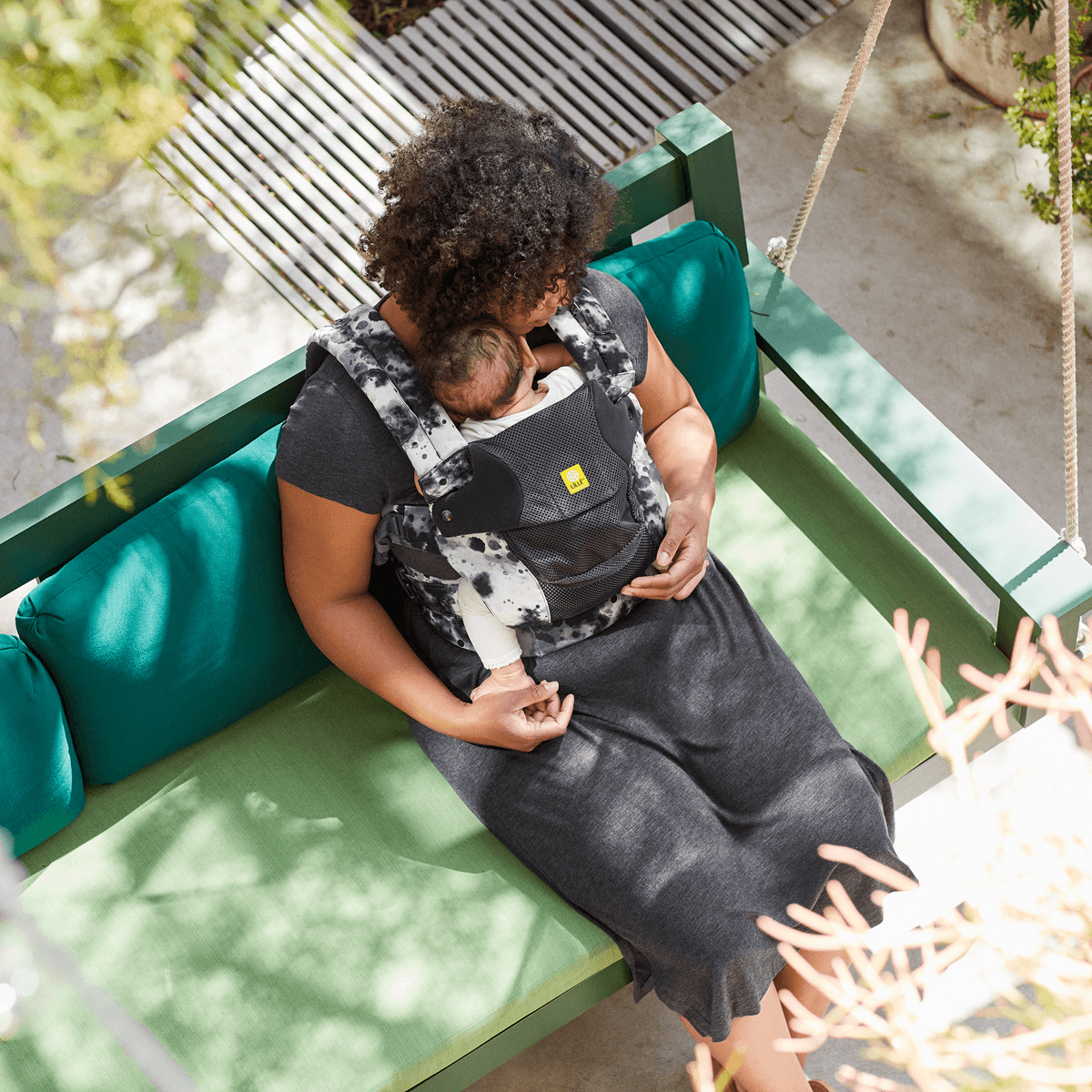 Mother sitting on an outdoor sofa with baby in a black and white carrier