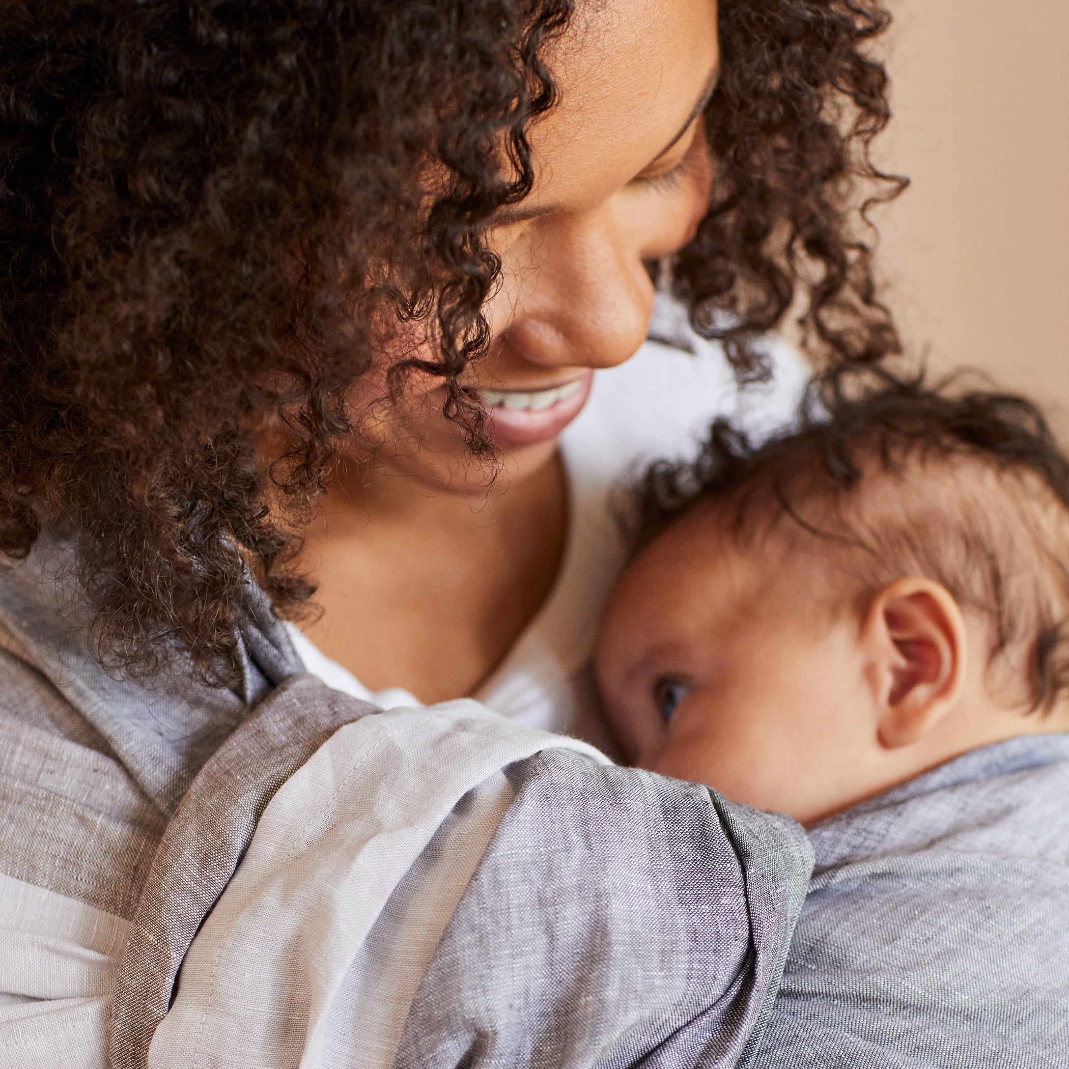 A woman smiling at her baby is wearing a Ring Sling in color Nimbus Cloud. The baby has their head rested on woman's chest.