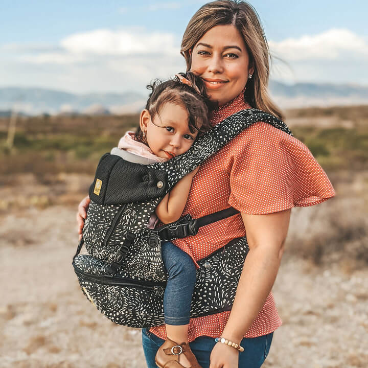 Mom holding her daughter in the LILLEbaby SeatMe carrier outdoors in the sand