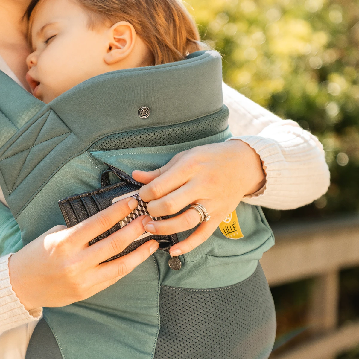 close up image of mom wearing baby in CarryOn Airflow DLX in Willow while she puts in her card wallet in the pocket of a carrier