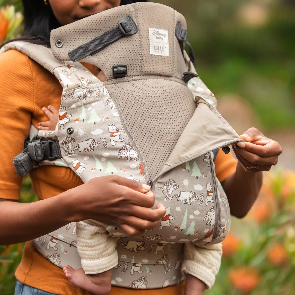 mom wearing baby in Complete 6-in-1 All Seasons in Pooh's Perfect Day baby carrier while opening the front zipper of the carrier
