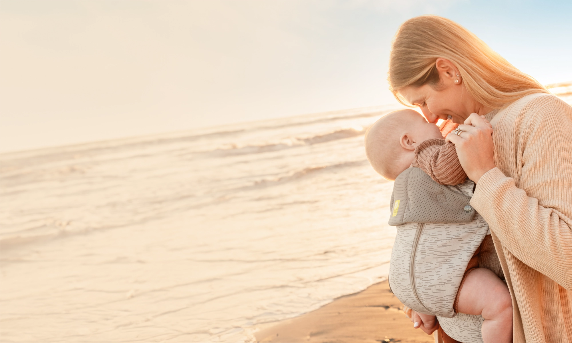 mom caressing baby while wearing the complete all seasons carrier in coastal sands