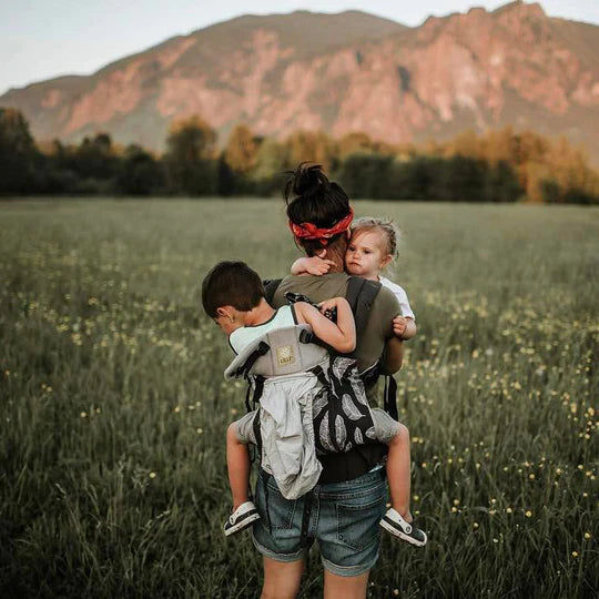 Mom with red headband carrying 2 kids in field