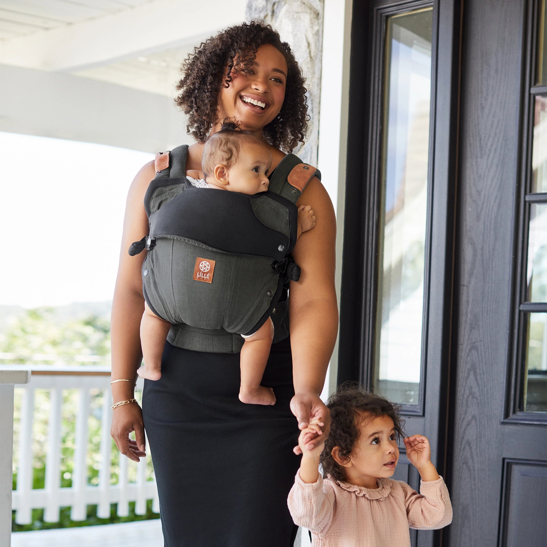 Elevate ergonomic carrier shown on plus size mom exiting the house with toddler.