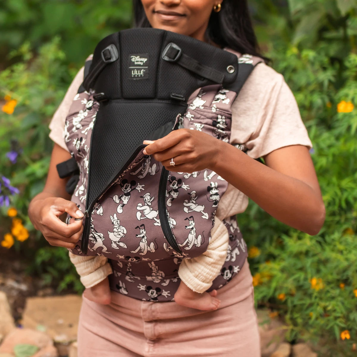 mom wearing baby in the Complete 6-in-1 All Seasons in Mickey & Friend's Jamboree baby carrier while opening the front zipper of the carrier