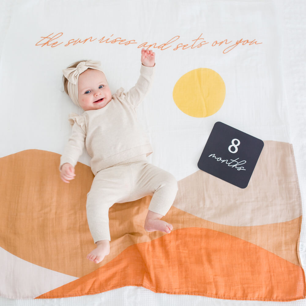8 month old baby on lulujo's blanket in butterscotch sunrise pattern
