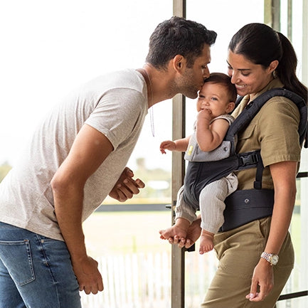 mom wearing lillebaby baby carrier while dad kisses baby on forehead