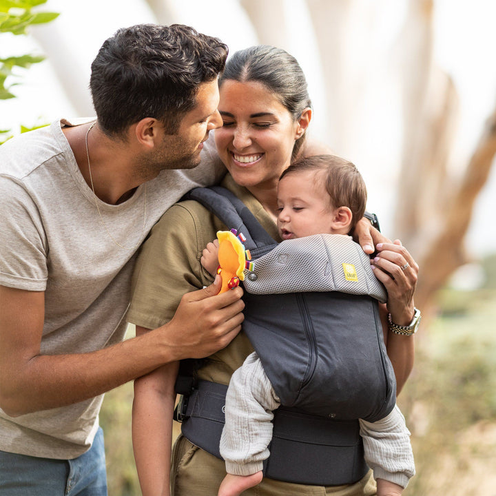 mom wearing lillebaby complete all seasons baby carrier in charcoal silver while dad hugs mom from back