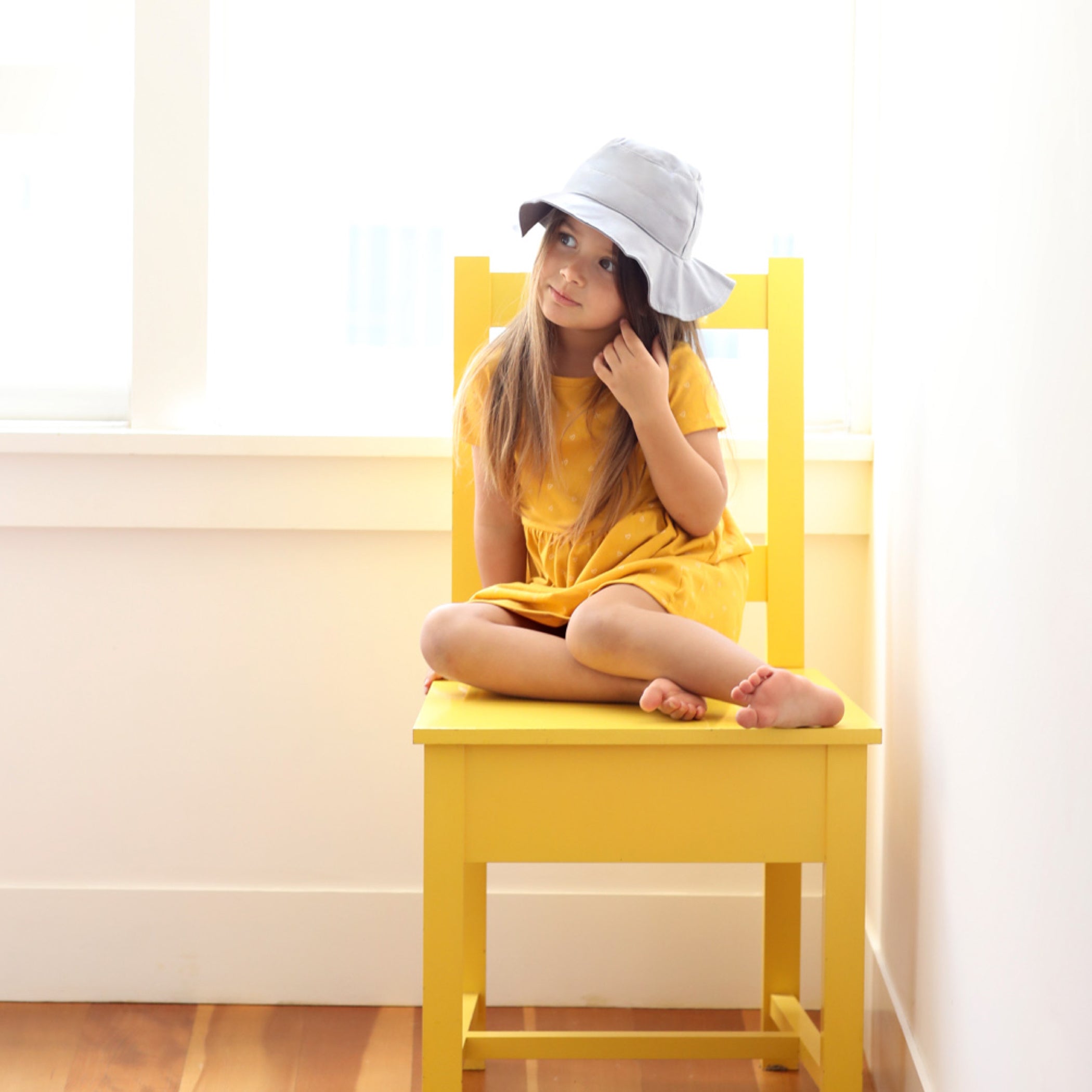 toddler girl wearing a gray bucket hat while sitting on a yellow chair
